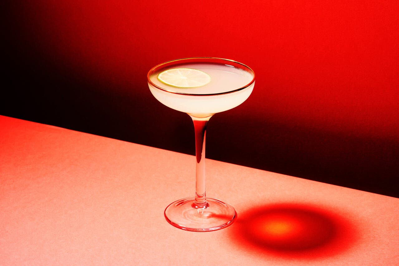 A Vodka Gimlet cocktail made of lime and gin in high glass on pink table against red background