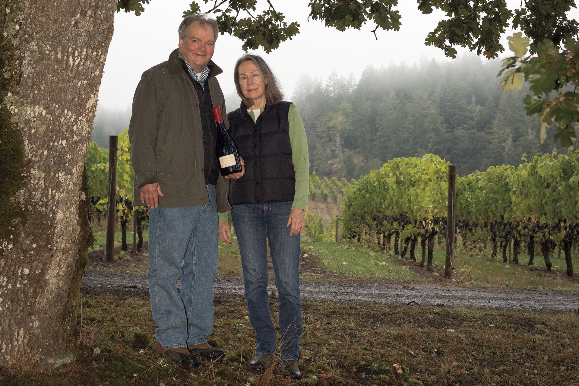 Dick and Deirdre Shea standing under a tree in front of a vineyard